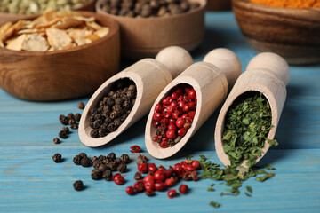 Scoops with different spices on light blue wooden table