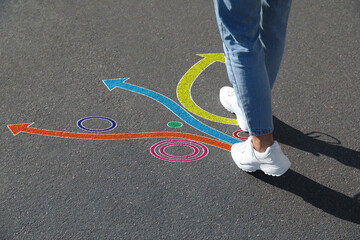Choice of way. Woman walking towards drawn marks on road, closeup. Colorful arrows pointing in...