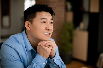 Dreamy middle aged asian businessman thinking of new business strategy, looking aside and smiling, free space