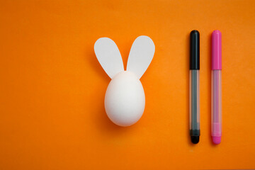 White chicken egg with paper rabbit ears on an orange background. Coloring book for children for...