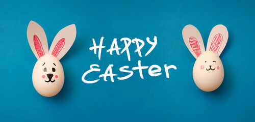 Food photo for Easter holiday. Chicken eggs with cute rabbit faces and bunny ears on a blue background. Easter coloring book for kids. Greeting card. Text Happy Easter. Copyspace. Banner. Handwritten