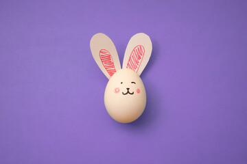 Food photo. White chicken egg with cute rabbit face and bunny ears on a purple background. Greeting card for religious holiday Happy Easter. Preparation for the celebration. Banner. Copyspace. Poster