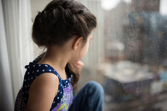 Thoughtful girl looking though wet window at home