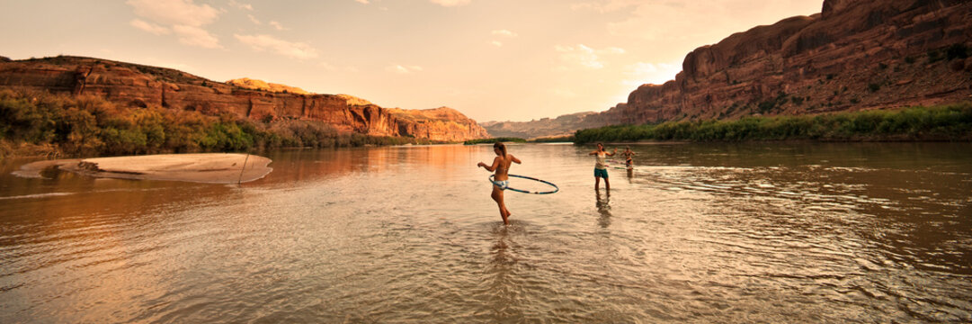 Three women playing and hula hooping in a shallow river at sunset.