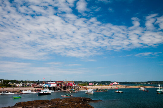 A red building on the edge of a small harbor with boats floating on a sunny day.