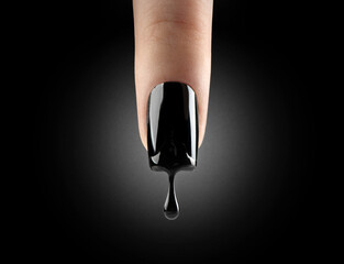 Nail art. Black gel polish dripping from beautiful long nail over black background. Woman finger...