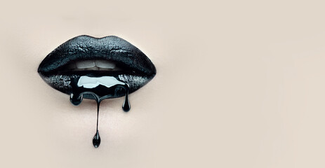 Black Paint dripping from the lips, dark liquid drops on beautiful model girl's mouth on beige background. Halloween party make-up, gothic style. Beauty makeup close up. Wide screen art backdrop.  - 561658831