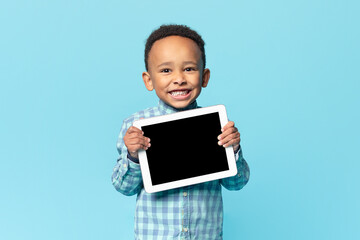 Cute african american kid boy holding digital tablet with blank black screen, recommending new app...