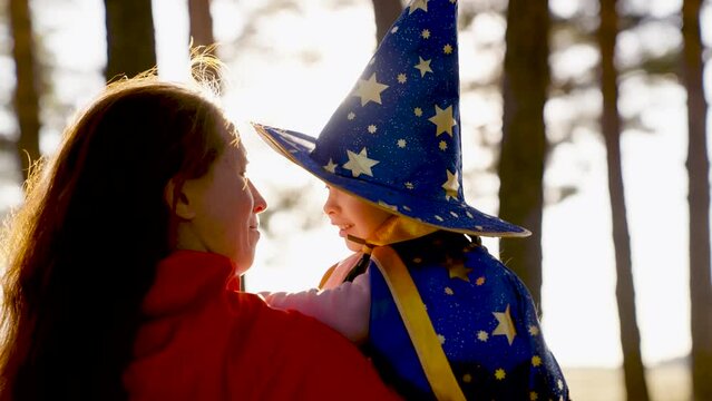 Happy family, Child plays in mantle of magician, mother in red cloak. Childhood dreams, fantasies to become wizard, Child plays with his mother in costumes of wizard, playing in park on Halloween.