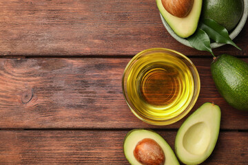 Cooking oil in bowl and fresh avocados on wooden table, flat lay. Space for text