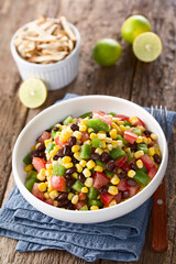 Mexican style colorful fresh vegetable salad made of beans, corn, tomato and bell pepper served in bowl, fork on the side, photographed on wood (Selective Focus, Focus on the front of the salad)