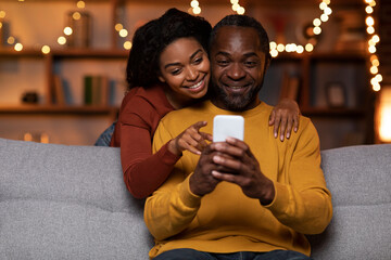Married black couple using cell phone at cozy winter evening