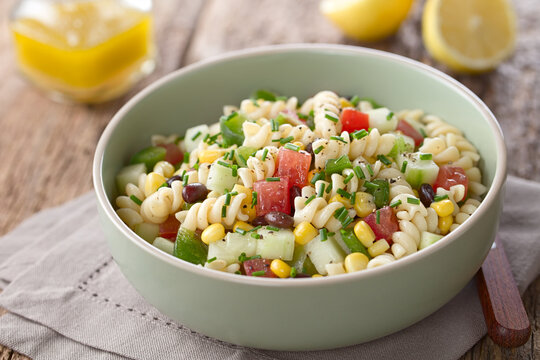 Fresh homemade colorful vegan fusilli pasta salad with beans, corn, tomato, cucumber and green bell pepper, photographed on wood (Selective Focusone third into the salad)