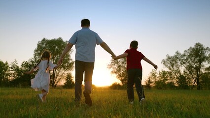 Naklejka na ściany i meble Summer, family walks outdoors holding hands. Family Teamwork. Weekend with family. Silhouette, happy running kids, dad, nature. Father, son, daughter play, run on green grass, hold hands in park