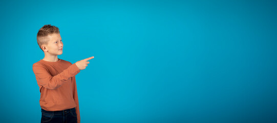 Cute smiling preteen boy pointing aside at copy space on blue background