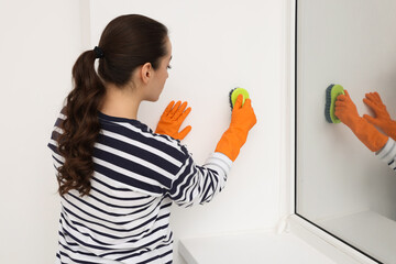Woman in rubber gloves cleaning wall with brush indoors