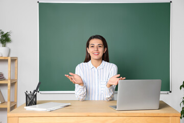 Happy young teacher explaining something at table in classroom