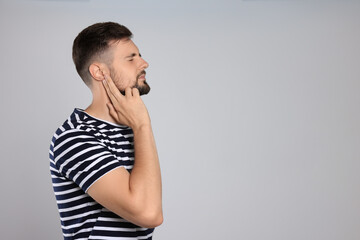 Young man suffering from ear pain on light grey background. Space for text