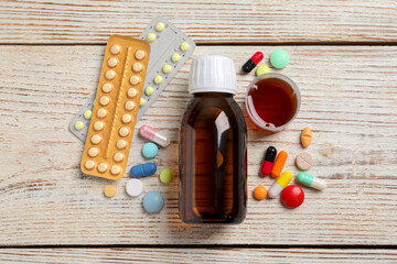 Bottle of syrup, measuring cup and pills on white wooden table, flat lay. Cold medicine