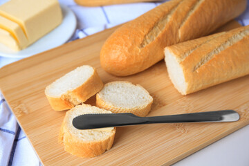 Tasty cut baguette with fresh butter on white table