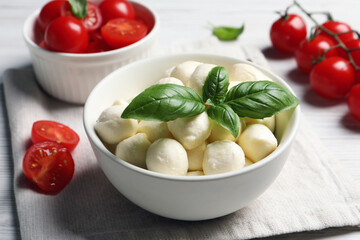 Delicious mozzarella balls, tomatoes and basil leaves in bowl on table, closeup