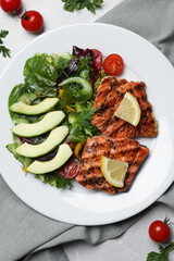 Tasty grilled salmon with avocado, lemon and tomatoes on light grey table, flat lay