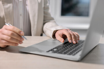 Woman with pen working on laptop at wooden table, closeup. Electronic document management