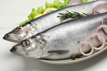 Plate with salted herrings, onion rings, slices of lemon, peppercorns and lettuce on white table,...