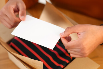 Young man holding greeting card near parcel with Christmas gift, closeup
