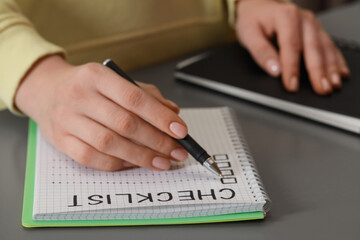 Fototapeta premium Woman filling Checklist with pen at grey table, closeup