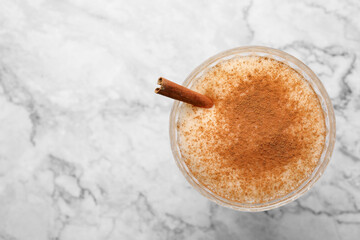 Delicious eggnog with cinnamon on white marble table, top view. Space for text