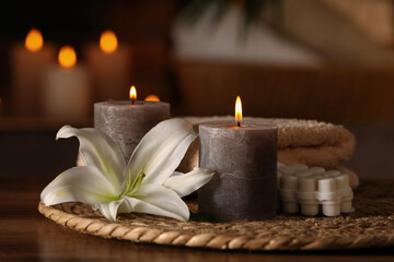 Fototapeta na wymiar Spa composition with burning candles, lily flower and towels on wooden table in wellness center