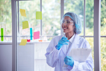 Woman scientist hand write note information in medical lab look at science microscope medical test, research biology chemistry. Asian Females technician laboratory analyzing blood test pharmaceutical