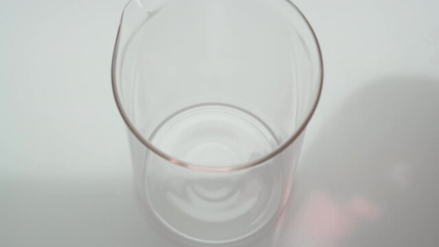 Macro crane shot of rose oil is being poured into empty beaker on grey background | Abstract cosmetics ingredients formulating concept