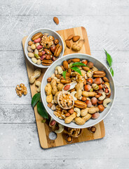 Different types of nuts in bowls with green leaves.