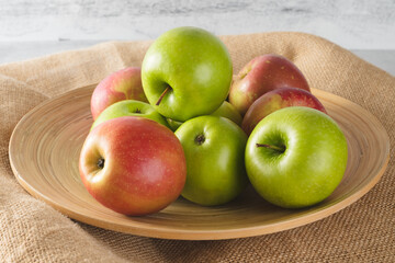 Red and green apples on a wooden plate close-up