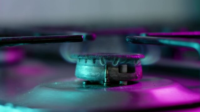 Close up view of old gas stove, fire starts to burn. Violet and blue light in kitchen shines on burner. Sanctioned gas in European family, lack of heat and heating.