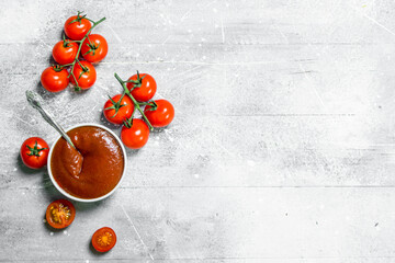 Tomato sauce in bowl with spoon and fresh tomatoes.