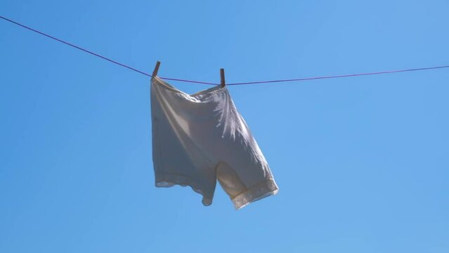 vintage white knickers are drying on a rope against the sky, swaying in the wind. slow motion.