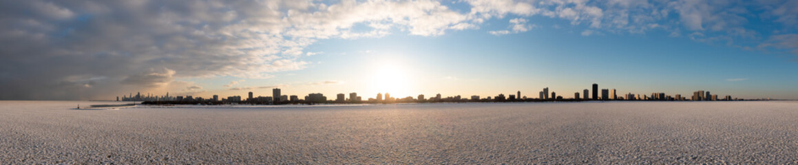Wide angle aerial panorama of Chicago lakefront from the Edgewater neighborhood extending to Evanston on the right and downtown Chicago on the Left with clouds above and ice and snow below at sunset.