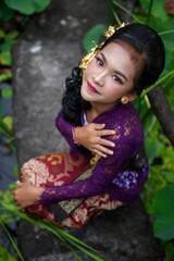 Naklejka premium Beautiful girl with long curly hair, makeup and purple shirt posing in the tropical garden
