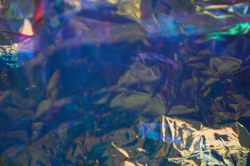 Holographic uneven, crumpled mother-of-pearl foil. Holographic iridescent abstract foil background. Unfocused background in blue tones. High quality photo