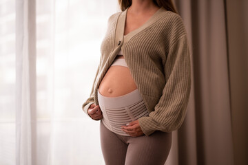 Unrecognizable pregnant woman touching baby bump, belly near window, cropped shot,Pastel colours.Natural,healthy,beautiful pregnancy concept.Copyspace for text. 