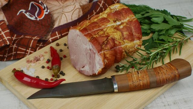 A piece of juicy and tasty bacon on a wooden cutting board with a carving knife, multi-colored allspice peas, red hot peppers, parsley, dill and basil. The concept of different meat preparation
