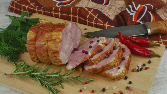 Traditional ham sliced on a wooden cutting board with a carving knife, multi-colored allspice, red hot peppers, parsley, dill and basil. The concept of snacks from pork meat
