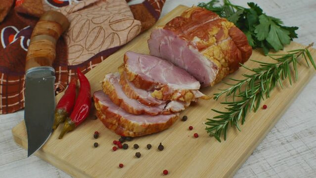 Traditional ham sliced on a wooden cutting board with a carving knife, multi-colored allspice, red hot peppers, parsley, dill and basil. The concept of snacks from pork meat
