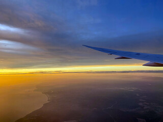 Though the window view over the wing of Aircraft air plane flying high altitude horizon and cloud daylight golden yellow sky 