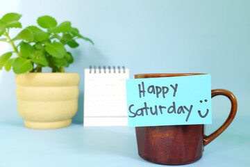Welcome, hello and happy Saturday concept. Selective focus of coffee cup with blue paper note and written message.