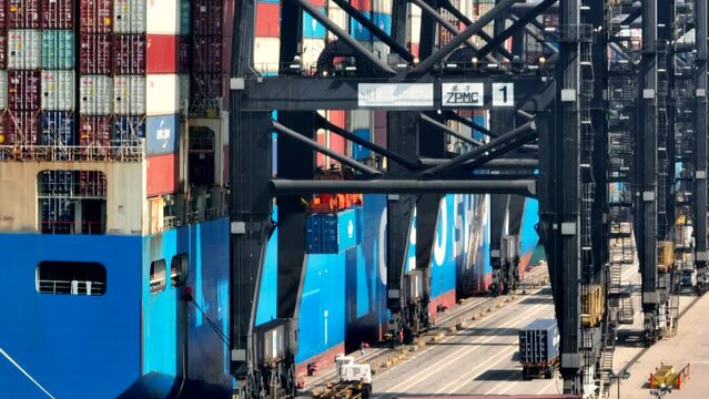 Gantry crane loading a blue container on a vessel. Rising following shot