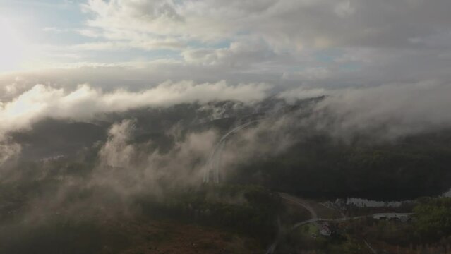 Drone footage of highway, and housing estate in Norway with some fog floating in the air and sun lighting up the clouds